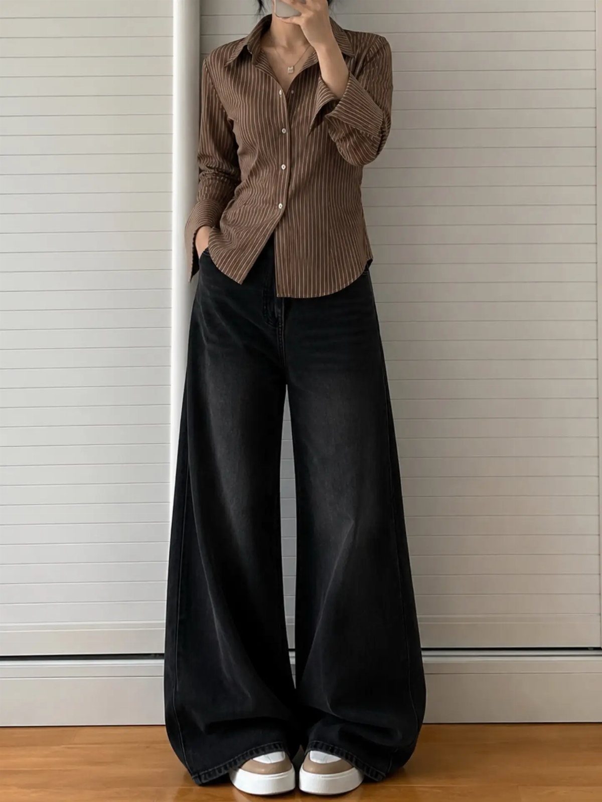 Person wearing a brown pinstriped shirt and very wide-leg black denim jeans.
