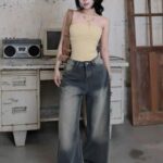 A young woman wearing a yellow tube top and wide-leg ombre jeans posing indoors.