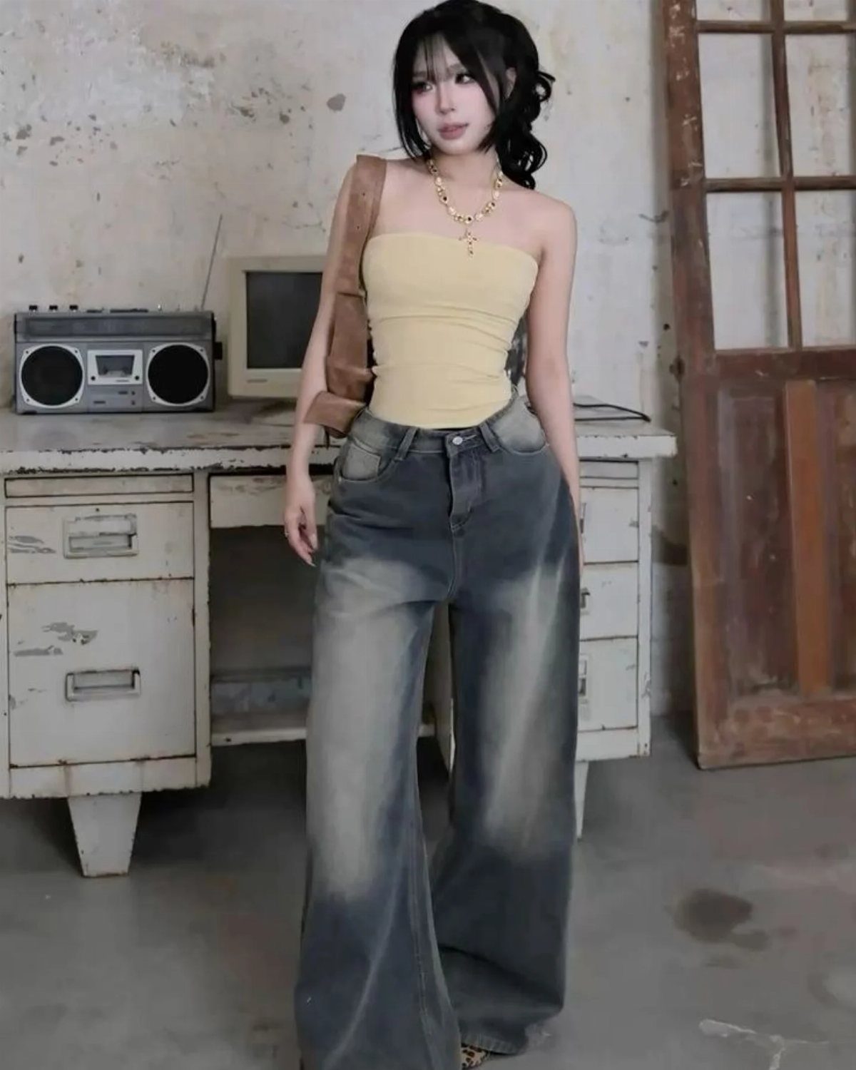 A young woman wearing a yellow tube top and wide-leg ombre jeans posing indoors.