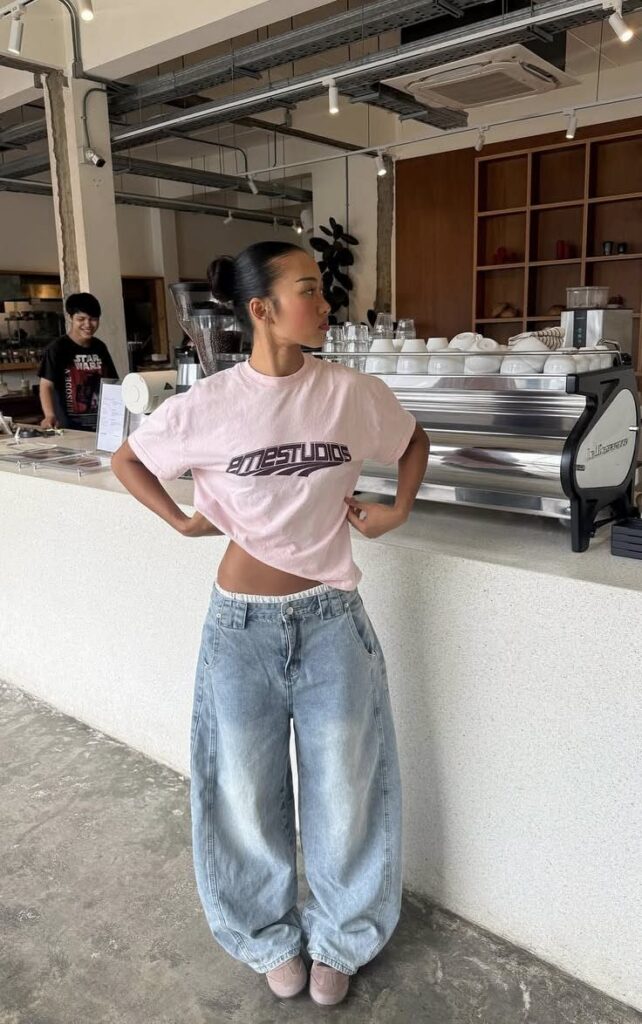 A woman posing in a pink cropped t-shirt and baggy light blue denim jeans.