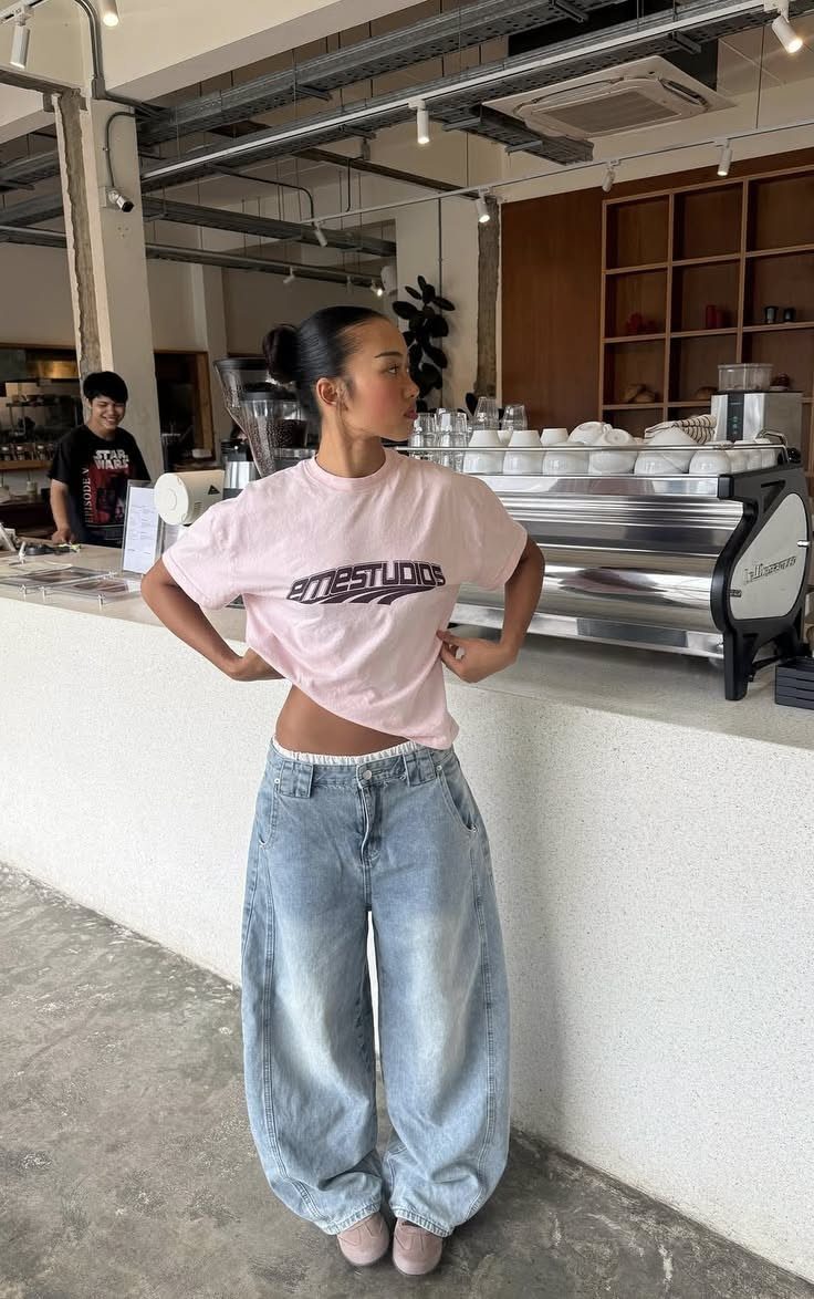 A woman posing in a pink cropped t-shirt and baggy light blue denim jeans.