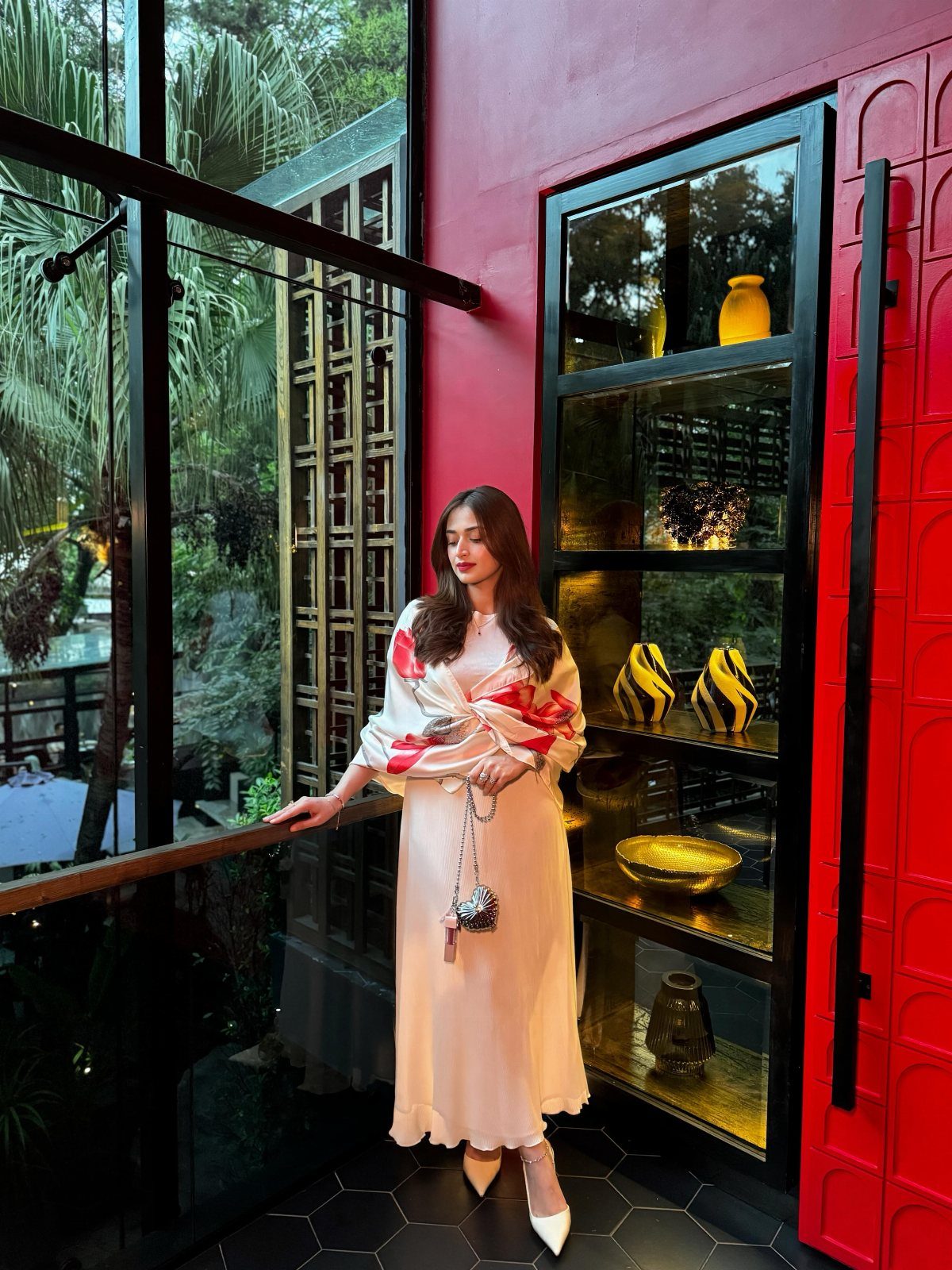 Woman in a cream satin midi dress and red wrap standing on a balcony.