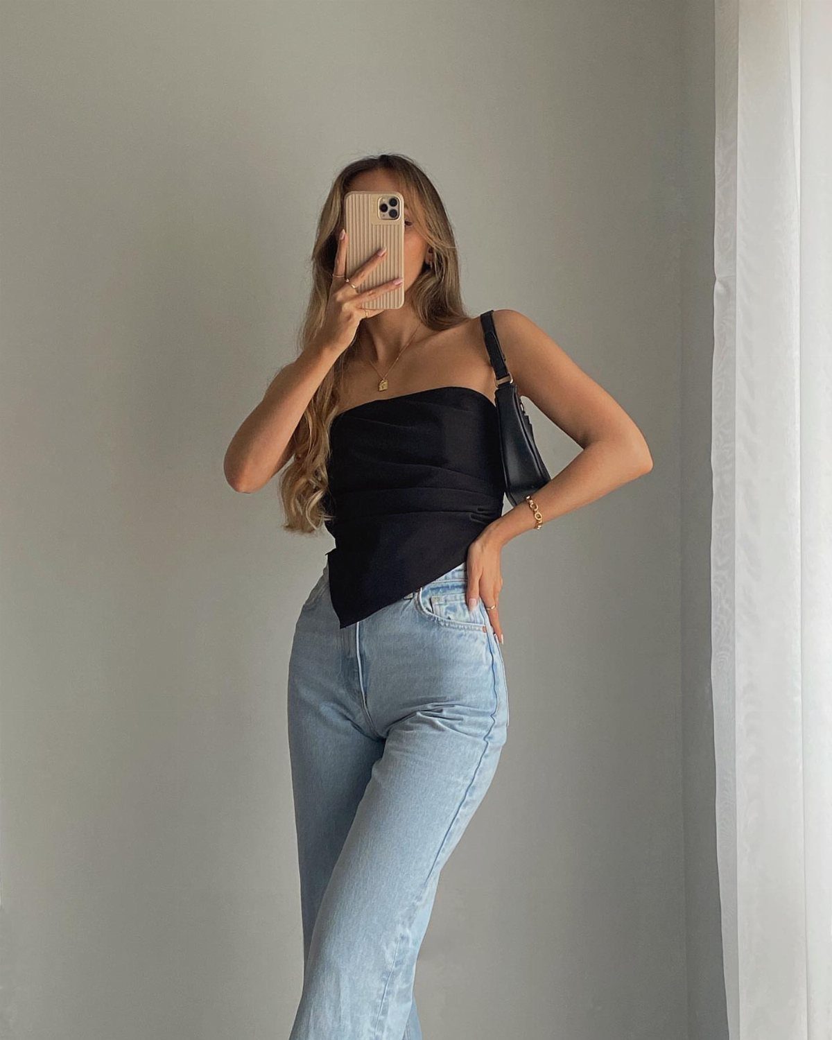 Woman in a black strapless top and light blue jeans posing for a mirror selfie.