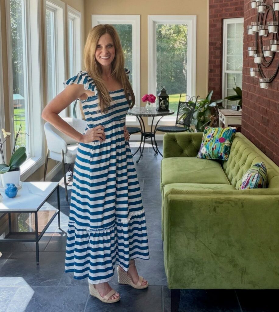A smiling woman posing in a blue and white striped maxi dress and wedge sandals.