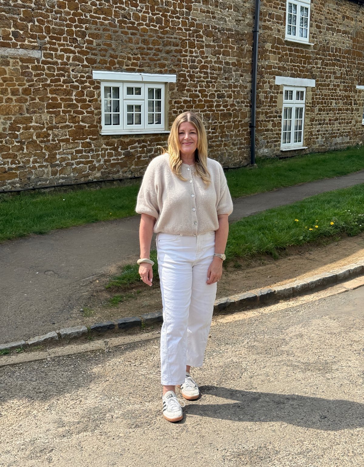 A woman wearing a cream short sleeve sweater and white trousers standing outdoors.