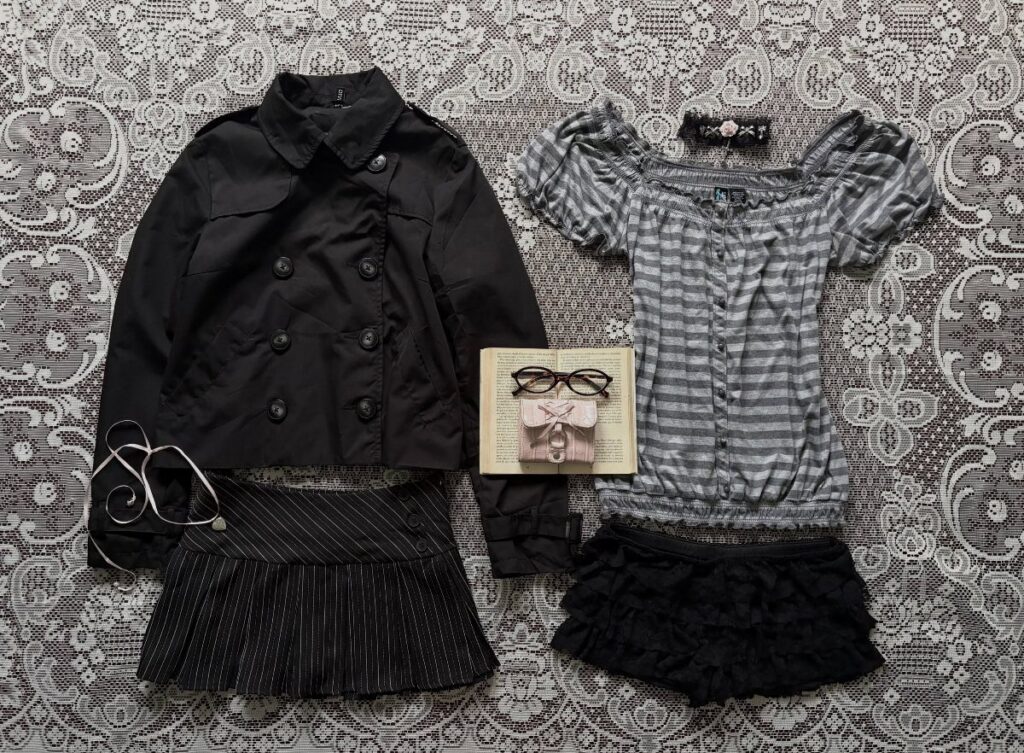 Black jacket, striped blouse, pleated skirt, and ruffled shorts laid out on lace fabric.