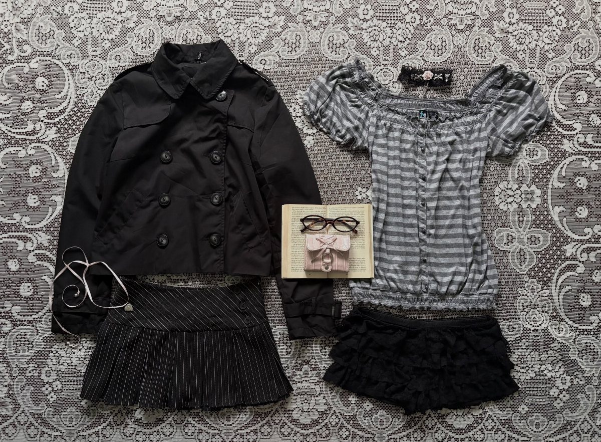 Black jacket, striped blouse, pleated skirt, and ruffled shorts laid out on lace fabric.