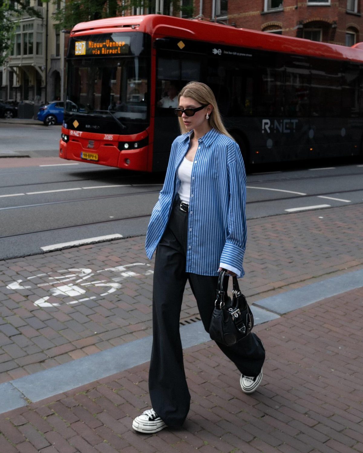 A woman in a blue striped shirt and black wide-leg trousers walking on a city street.