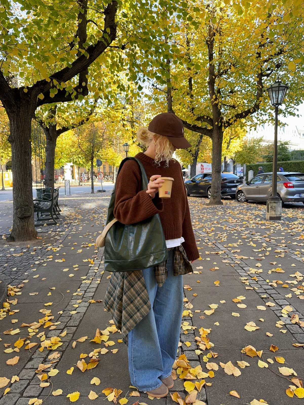 Person in a brown knit sweater and wide-leg jeans walking through autumn leaves.