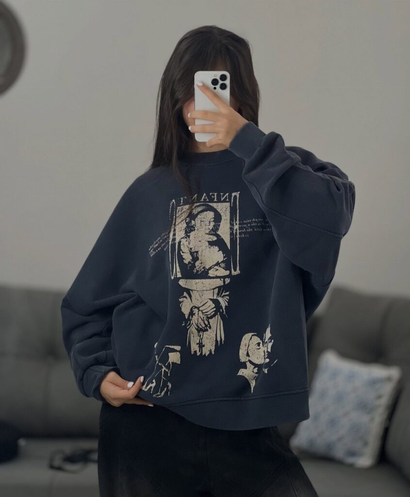 A person posing in a dark navy oversized graphic sweatshirt while holding a smartphone.