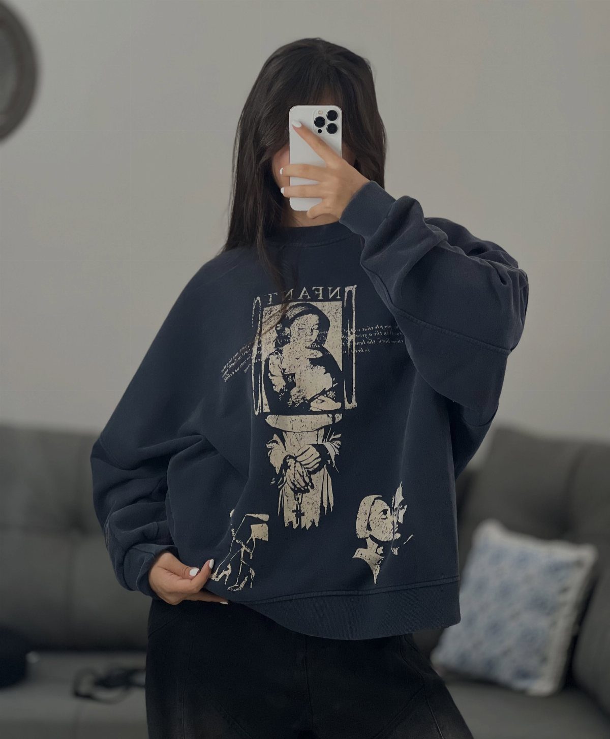 A person posing in a dark navy oversized graphic sweatshirt while holding a smartphone.