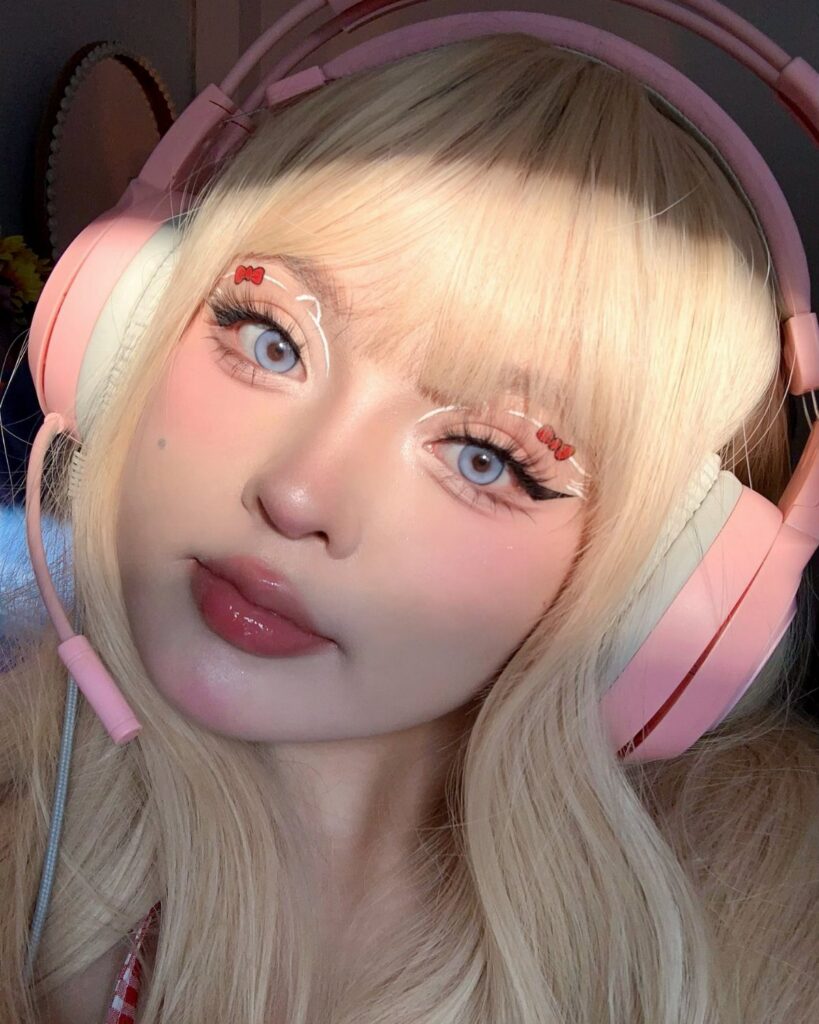 Blonde person wearing pink headphones with glossy pink lips and decorative eye makeup.