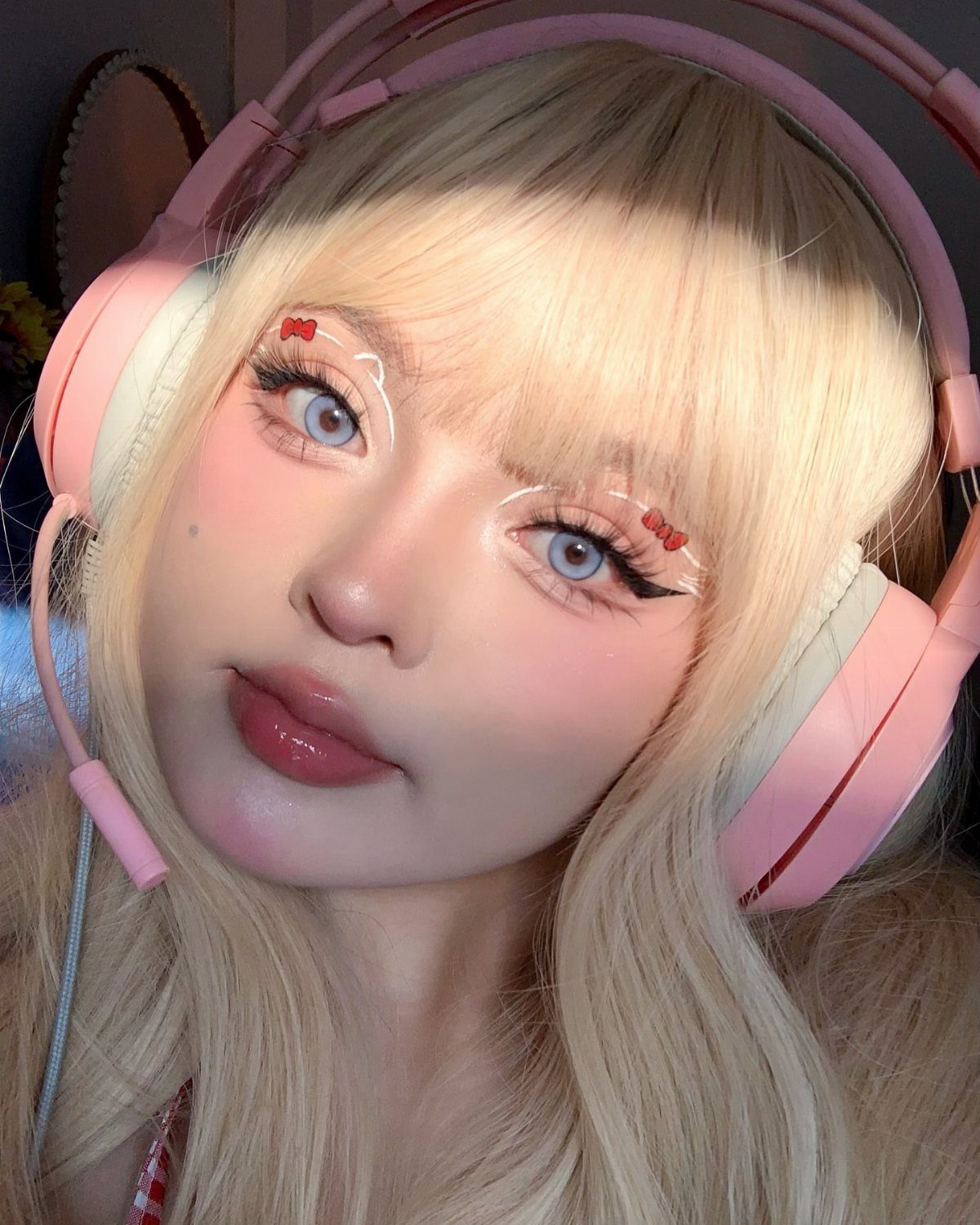 Blonde person wearing pink headphones with glossy pink lips and decorative eye makeup.