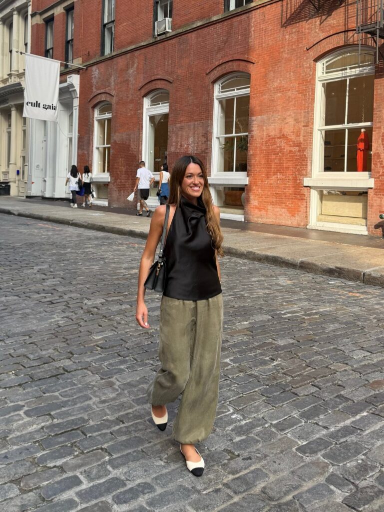 A woman in a black halter top and olive trousers walking on a cobblestone street.
