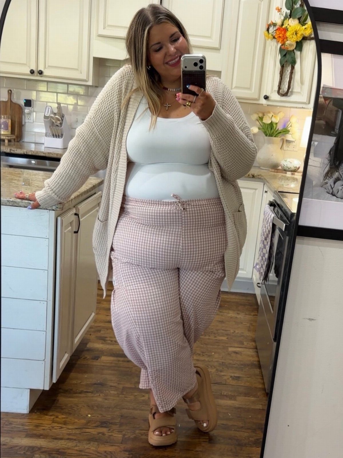 Woman in pink gingham pants and white tank top posing for a mirror selfie.
