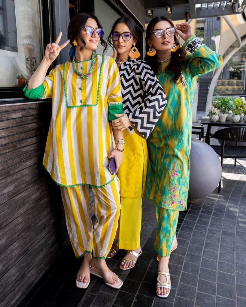 Three women posing in vibrant, colorful patterned tunic and matching pant sets outdoors.