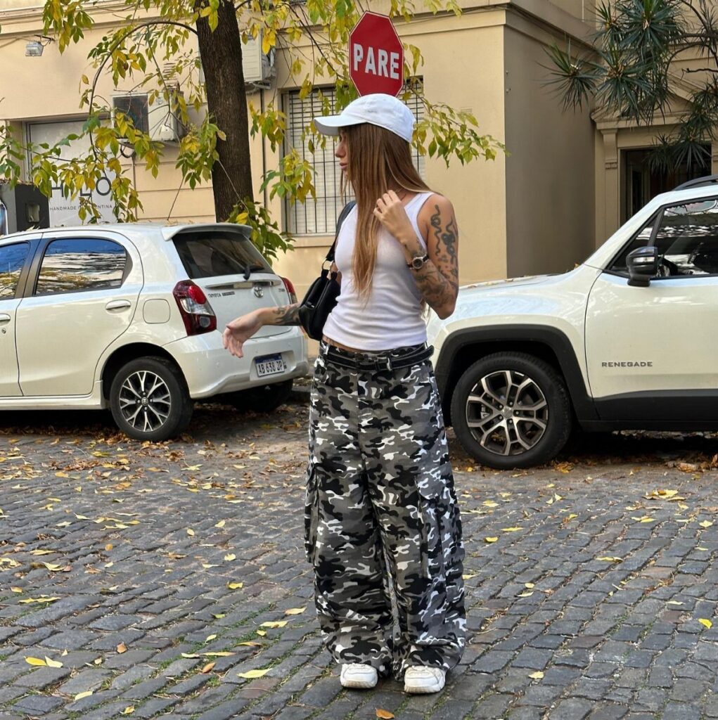 A woman wearing camouflage wide-leg cargo pants and a white tank top standing on a cobblestone street.