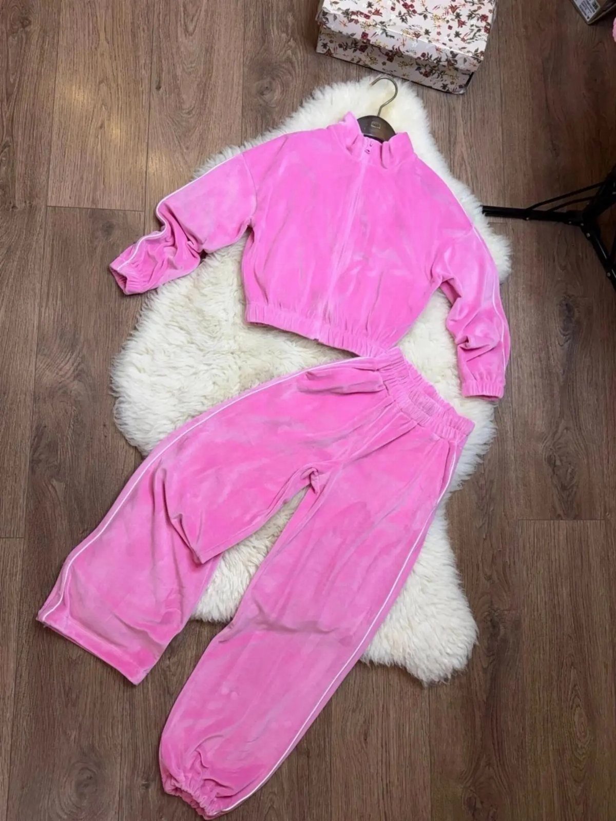 Pink velour tracksuit jacket and matching pants laid on a white faux fur rug.
